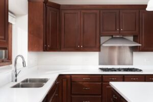 Traditional kitchen with deep cherry wood cabinets, raised panel doors, white countertops, stainless steel range hood, and double sink