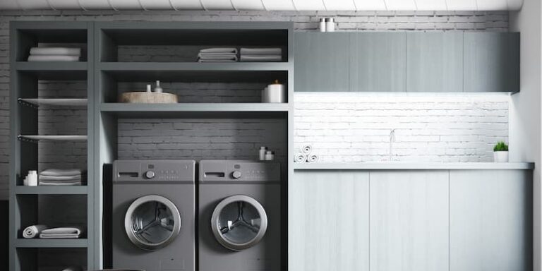 A modern laundry room featuring built-in gray shelving, side-by-side front-load washer and dryer, and sleek light blue cabinetry with a white brick tile backsplash.