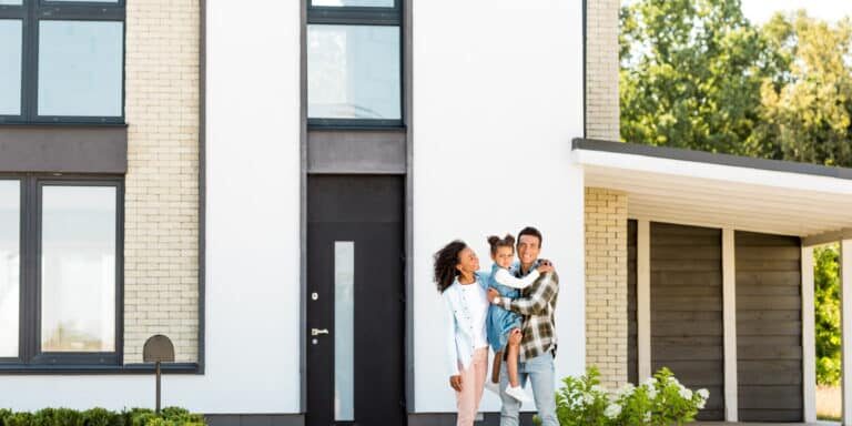 full length view of african american family standing near new house while father holding kid Young family smiling in front of their house.jpeg
